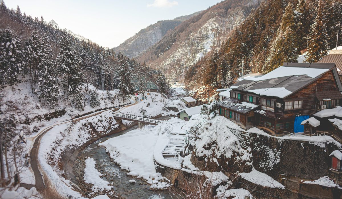 High angle shot of a wooden house surrounded by forested mountain covered in snow in winter